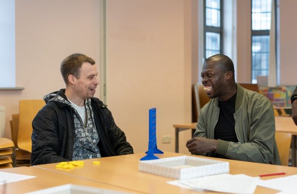 Two people sit in a room and play a game together at a table